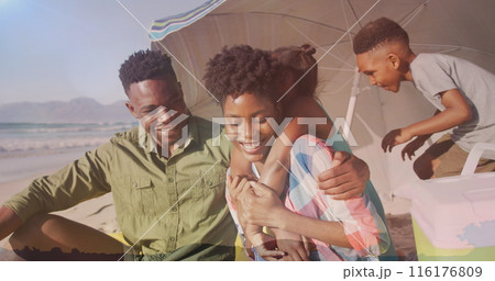 Black family enjoys beach; dad hugs mom, children play 116176809