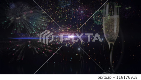 A glass of champagne standing with fireworks bursting in background 116176918
