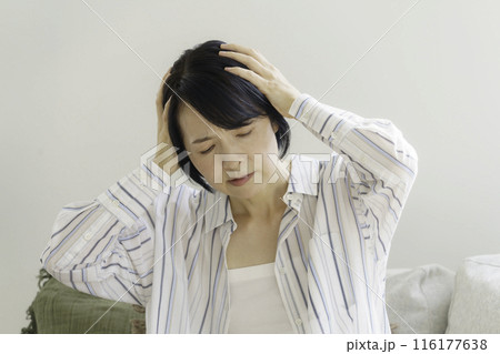 ソファに座る頭をおさえるミドルエイジの女性　頭痛 116177638