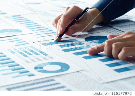 経営分析のイメージ。経営戦略を考えるコンサルタント。多数のレポートの中のグラフを指さすアナリストの手 116177976