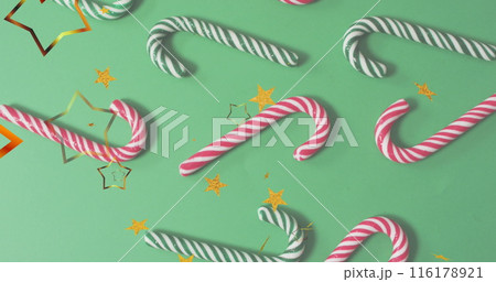 Image of happy holidays text and stars over candy canes on green backrgound 116178921