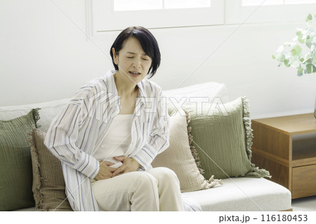 ソファに座ってお腹をおさえるミドルエイジの女性 腹痛 ソファに座ってお腹をおさえるミドルエイジの女性 腹痛 116180453