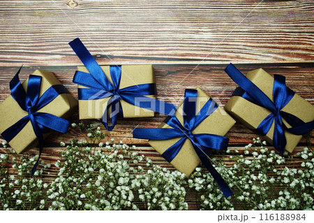 Gift boxes with blue ribbon and flower decoration on wooden background 116188984