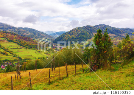 mountainous rural scenery with fence on the hill. countryside landscape with rolling hills and village in the valley. cloudy autumn weather mountainous rural scenery with fence on the hill. countryside landscape with rolling hills and village in the valley. cloudy autumn weather 116190350