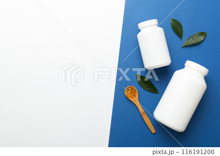 Omega-3 capsules lie in white bottle on a table with green leaves background. Fish oil tablets. Biologically active additives. omega 6, omega 9, vitamin A, E, D, vitamin D3 top view with copy space 116191200
