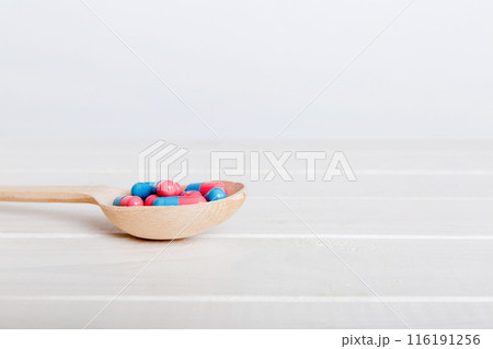 Vitamin capsules in a spoon on a colored background. Pills served as a healthy meal. Red soft gel vitamin supplement capsules on spoon 116191256