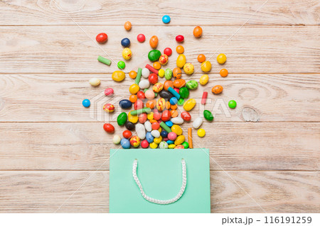 shopping paper gift bag in corner full of assorted traditional candies falling out on colored background with copy space. Happy Holidays sale concept 116191259