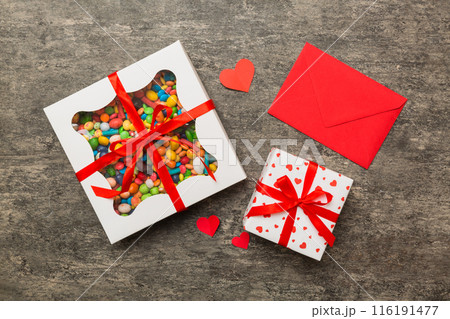 Red envelope with candy and gift box and Valentines hearts on colored background. Flat lay, top view. Romantic love letter for Holiday concept Red envelope with candy and gift box and Valentines hearts on colored background. Flat lay, top view. Romantic love letter for Holiday concept 116191477