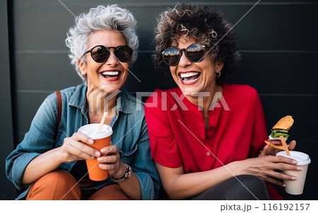 Couple of older lesbians eating street food and having fun while sitting in a cafe Couple of older lesbians eating street food and having fun while sitting in a cafe 116192157