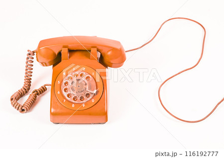 Vintage orange rotary dial telephone with a coiled cord, on a white background, studio shot. 116192777