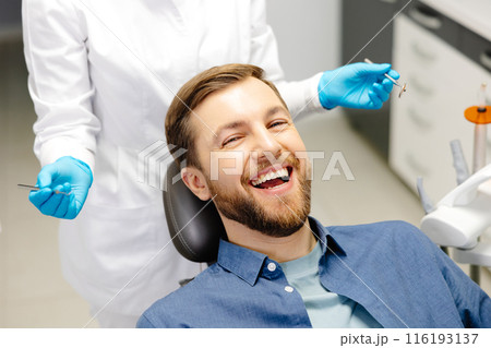 Portrait of happy man sitting at dentist chair in modern clinic and smiling. Patient enjoying dental treatment with professional dentist 116193137