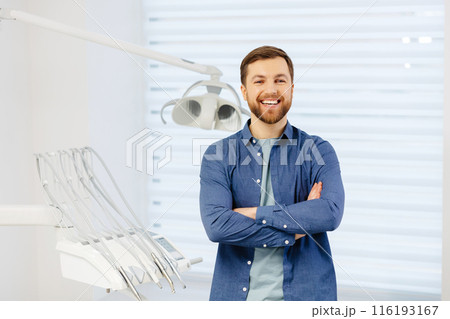 Confident male patient of stomatology standing in modern clinic. Man smiling at the camera crossing his arms in front of him 116193167