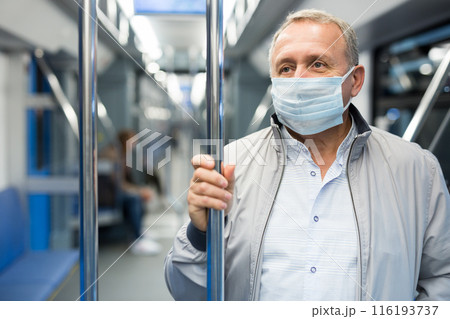 Mature passenger wearing protective mask rides in an underground metro car Mature passenger wearing protective mask rides in an underground metro car 116193737