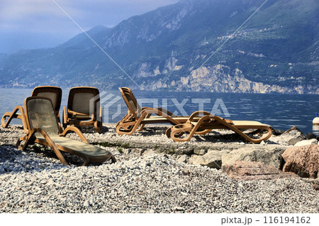 Empty Lounge Chairs Before the Start of the Holiday Season on a Pebble Beach at Lake Garda in Italy Empty Lounge Chairs Before the Start of the Holiday Season on a Pebble Beach at Lake Garda in Italy 116194162