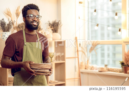 Dark-skinned man in eyeglasses working with pottery in his workshop Dark-skinned man in eyeglasses working with pottery in his workshop 116195595