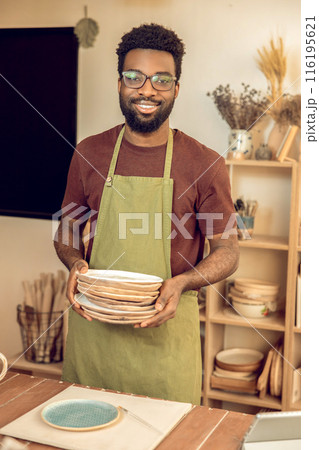 Man in apron standing with ceramic plates in hands Man in apron standing with ceramic plates in hands 116195621