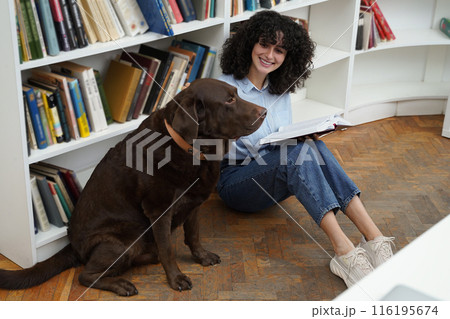 Curly-haired woman sitting on the floor in a library with a dog 116195674