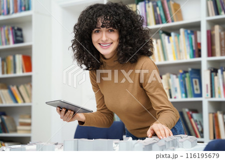 Curly-haired woman working on miniature project in a library 116195679