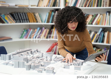 Curly-haired woman working on miniature project in a library 116195683