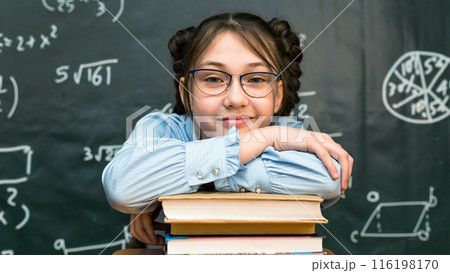 A schoolgirl girl put her hands and head on a stack of books in a school class 116198170