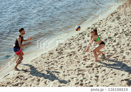 Aerial view on two young people, men and women in motion, playing beach volleyball with determination and motivation, enjoying early morning vibe 116198819