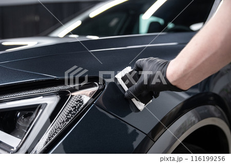 Mechanic wearing black gloves applying a protective coating to a car's front fender in a detailing studio 116199256
