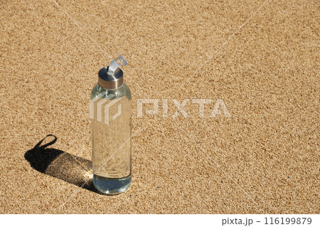 Transparent refreshing glass bottle of water in sunny day with hard shadow on outdoor beige sports ground with artificial covering. Concept water balance for heat season for workout. View from above Transparent refreshing glass bottle of water in sunny day with hard shadow on outdoor beige sports ground with artificial covering. Concept water balance for heat season for workout. View from above 116199879