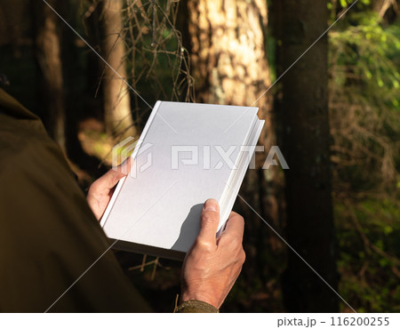 . Male hands holding book cover, blank hardcover mockup in nature. . Male hands holding book cover, blank hardcover mockup in nature. 116200255