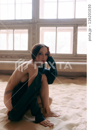 Woman in an unbuttoned jacket and jeans posing against a wall 116201030