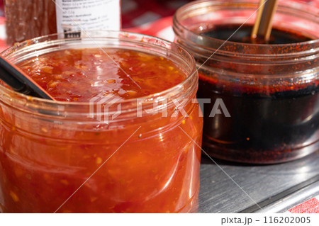 Two jars with red and dark sauces on a metal table, with spoons. Chunky, spicy red sauce and dark Two jars with red and dark sauces on a metal table, with spoons. Chunky, spicy red sauce and dark 116202005