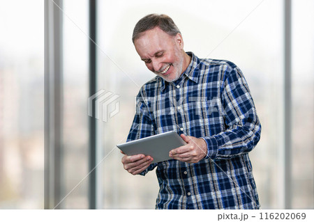 Smiling mature man holding tablet pc in both hands. Huge office windows background. Smiling mature man holding tablet pc in both hands. Huge office windows background. 116202069