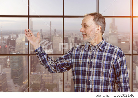 Handsome mature senior man presenting copy space with his hand. Checkered windows background with cityscape view. 116202146