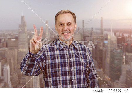 Happy confident mature man giving victory gesture sign. Urban cityscape background. 116202149