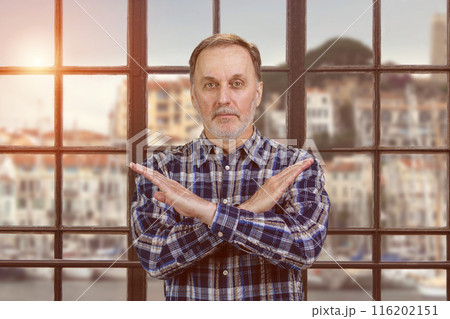 Portrait of a handsome serious man shows reject gesture with arms cross. Checkered windows backgorund with evening sunlight. Portrait of a handsome serious man shows reject gesture with arms cross. Checkered windows backgorund with evening sunlight. 116202151