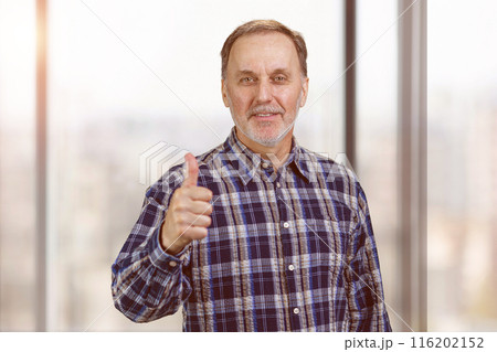 Smiling confident mature man giving his thumb up. Okay gesture sign. Office windows background. Smiling confident mature man giving his thumb up. Okay gesture sign. Office windows background. 116202152