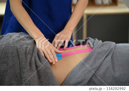 Rehabilitation specialist applying Kinesio tape on patient lower back. Alternative medicine concept 116202992