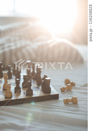 Chess board in sunlight on bed. Strategy thinking. Morning ideas concept. Pastel shades. Unmade bedding sheets and blanket 116208828