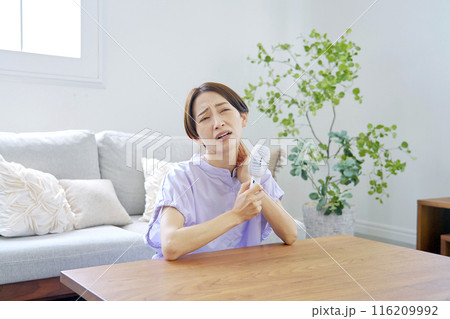 蒸し暑いリビングで携帯扇風機を使う女性 116209992