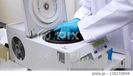 A person in lab coat and blue gloves is operating a centrifuge machine 116210694