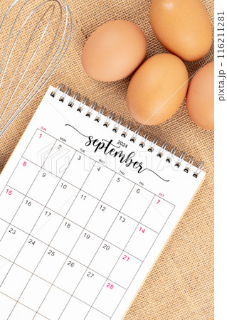September 2024 Desk calendar and fresh eggs with egg whisk on burlap 116211281