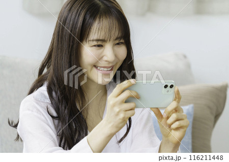 リビングで動画鑑賞する笑顔の若い女性　ビデオ通話 116211448