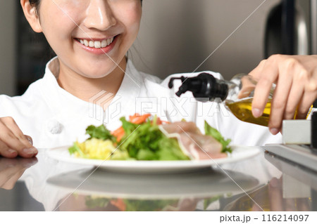 オリーブオイルをサラダにかける女性料理人 116214097