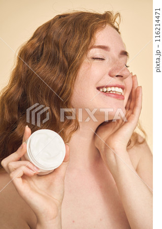 Woman Holding Skincare Cream and Smiling Radiantly with Closed Eyes 116214471