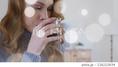 Image of light spots over caucasian woman drinking coffee in kitchen Image of light spots over caucasian woman drinking coffee in kitchen 116222634