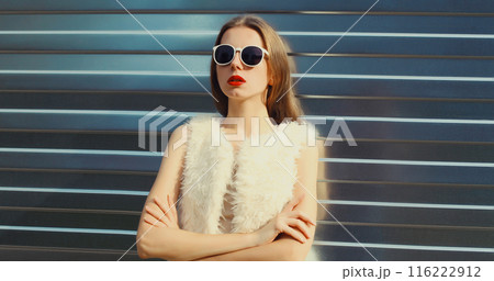 Modern stylish young woman in white fur vest, glasses, fashionable girl posing on gray background Modern stylish young woman in white fur vest, glasses, fashionable girl posing on gray background 116222912