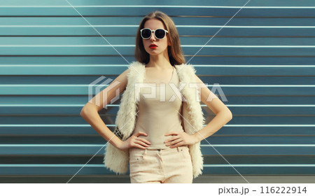 Modern stylish young woman in white fur vest, glasses, fashionable girl posing on gray background 116222914