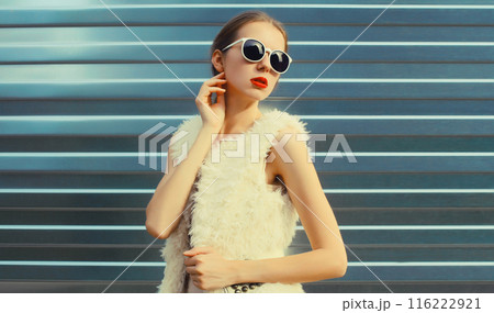 Modern stylish young woman in white fur vest, glasses, fashionable girl posing on gray background 116222921