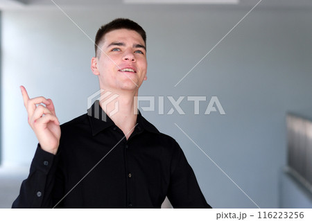 The young man in the shirt shows his finger on the empty space for copying the text while standing in modern office. Smiling handsome mixed race businessman looking at camera. Template for advertising 116223256