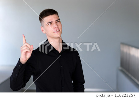 Index finger up attention. Handsome man with black hair and blue eyes. Mixed race nationality student or freelancer thinks questioningly and finding solution and typing on laptop Index finger up attention. Handsome man with black hair and blue eyes. Mixed race nationality student or freelancer thinks questioningly and finding solution and typing on laptop 116223257