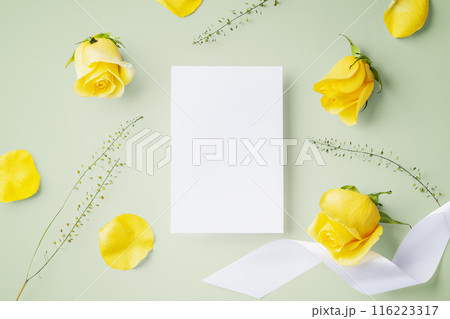 White card with yellow rose and ribbon on light green  background, top view 116223317